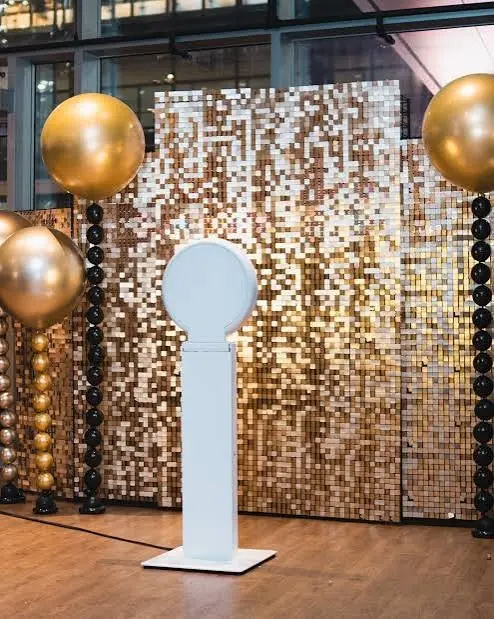 Photo booth with a white arch backdrop against a gold sequin shimmer wall and balloon columns
