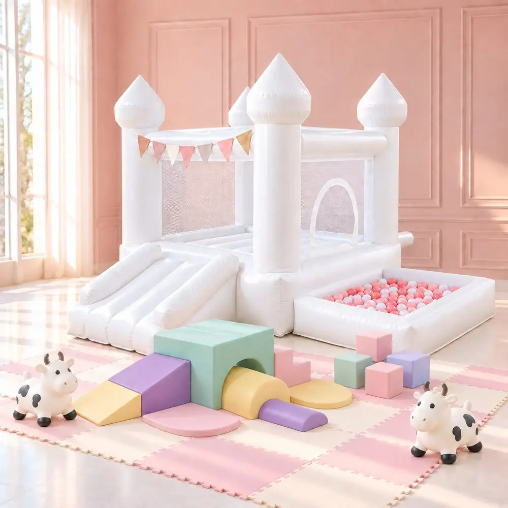 White bounce house castle with slide and ball pit next to a pastel foam climbing set, tunnel, and cow hopper toys on a play mat