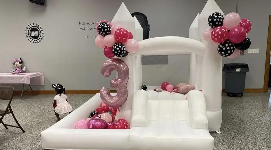 White bounce house with pink balloon clusters